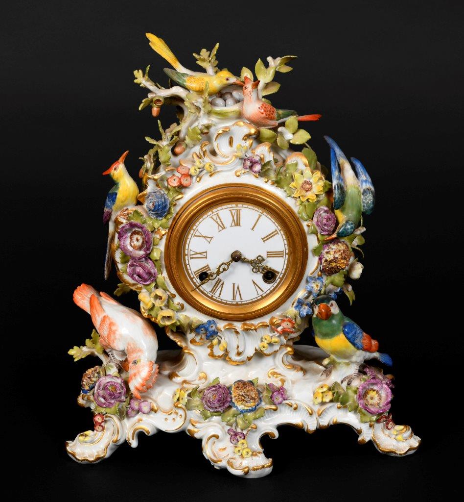 A cased Meissen clock with various birds including a parrot and cockatoo and birds on a rococo-style base