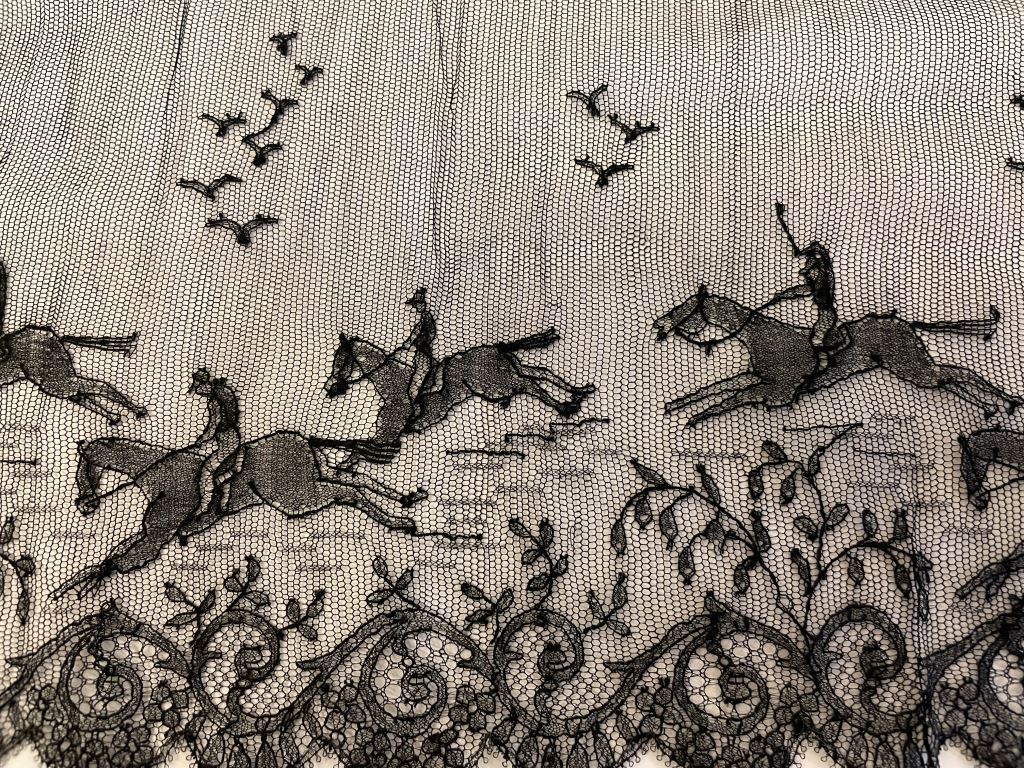 A detail of horse riders on Chantilly lace